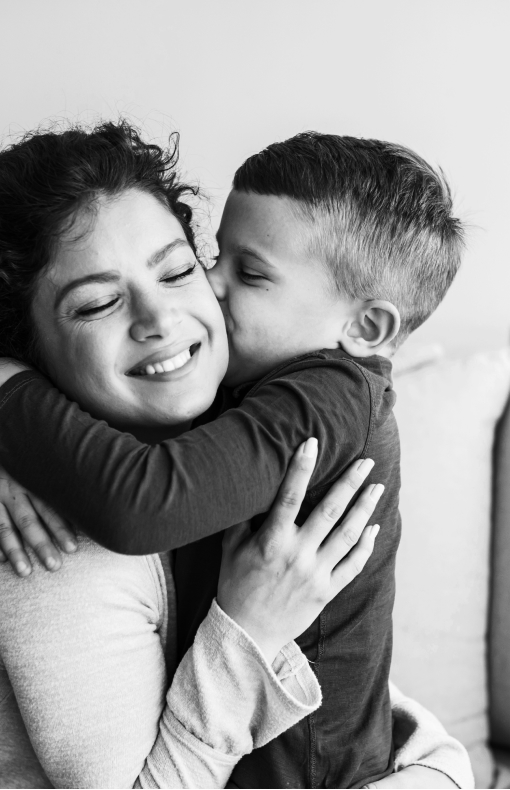 Mother smiling while holding her young son as he kisses her cheek