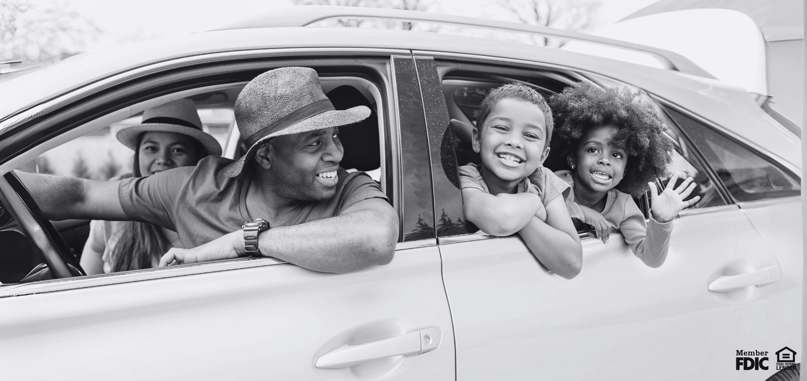 dad in the driver's seat looking back at his two kids waving from the back seat