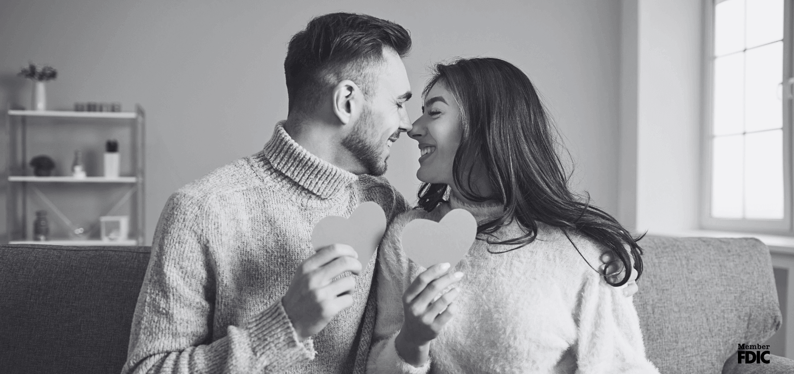 a couple rubs noes while holding paper hearts to show their love for eachother