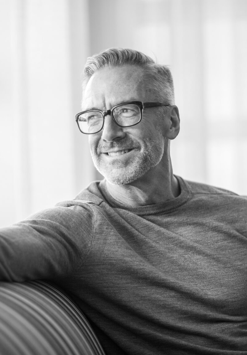 Mature man smiling on couch while looking out a window